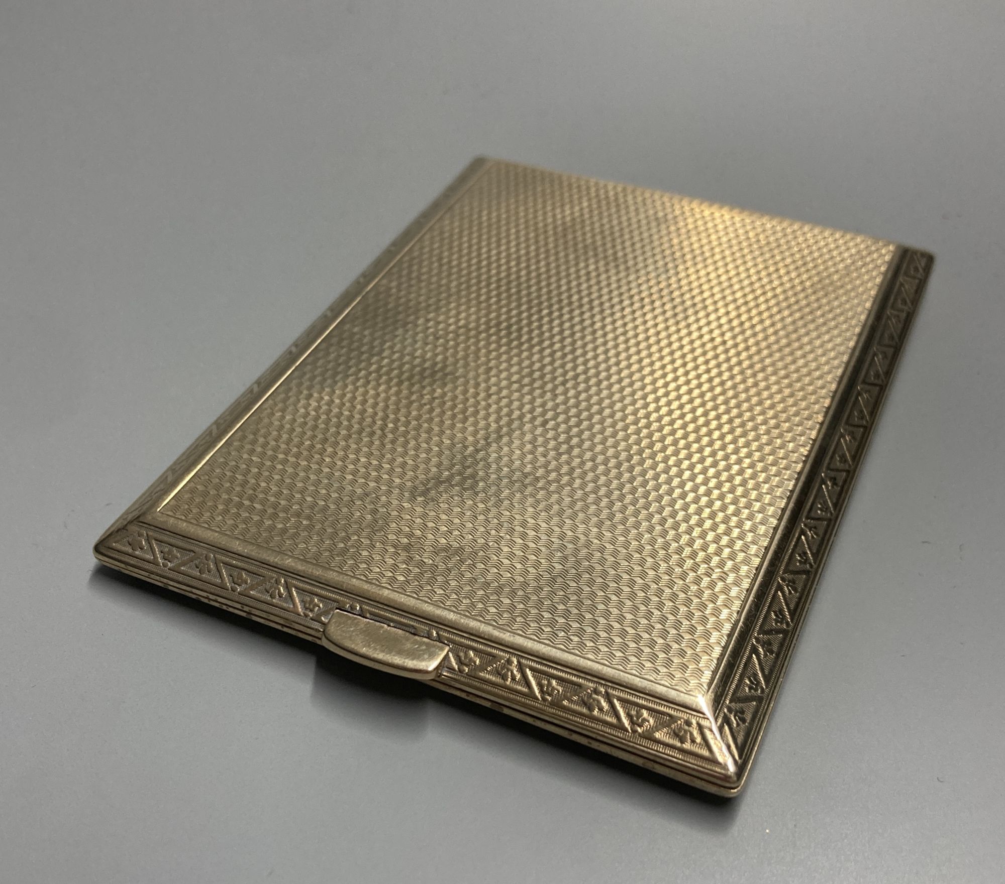 A late 1920s 9ct gold engine-turned cigarette case, with chased fleur-de-lys border, inscribed to interior, 11.3cm, gross 141g,